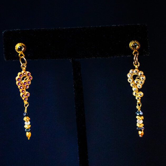 Luxury asymmetrical 18K gold earrings with diamonds, rubies, and blue sapphires.